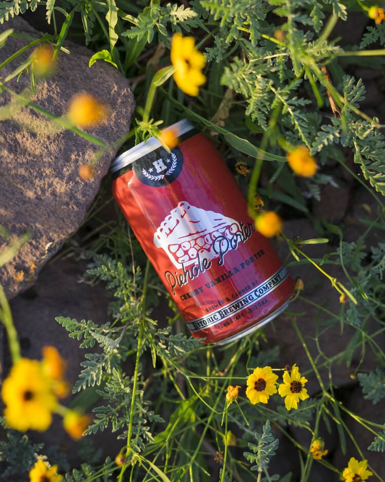 Can of Drive Thru Porter beer resting on grass and yellow flowers near rocks