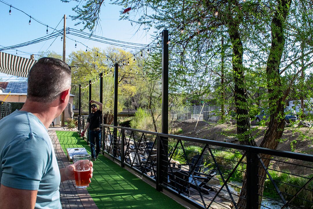 Founding Father patio-cornhole locals holding beers playing cornhole at Founding Fathers Collective Patio Area