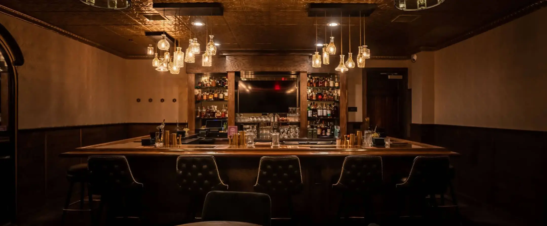Dimly lit bar at Founding Fathers Collective with tufted chairs, warm lighting, and stocked shelves