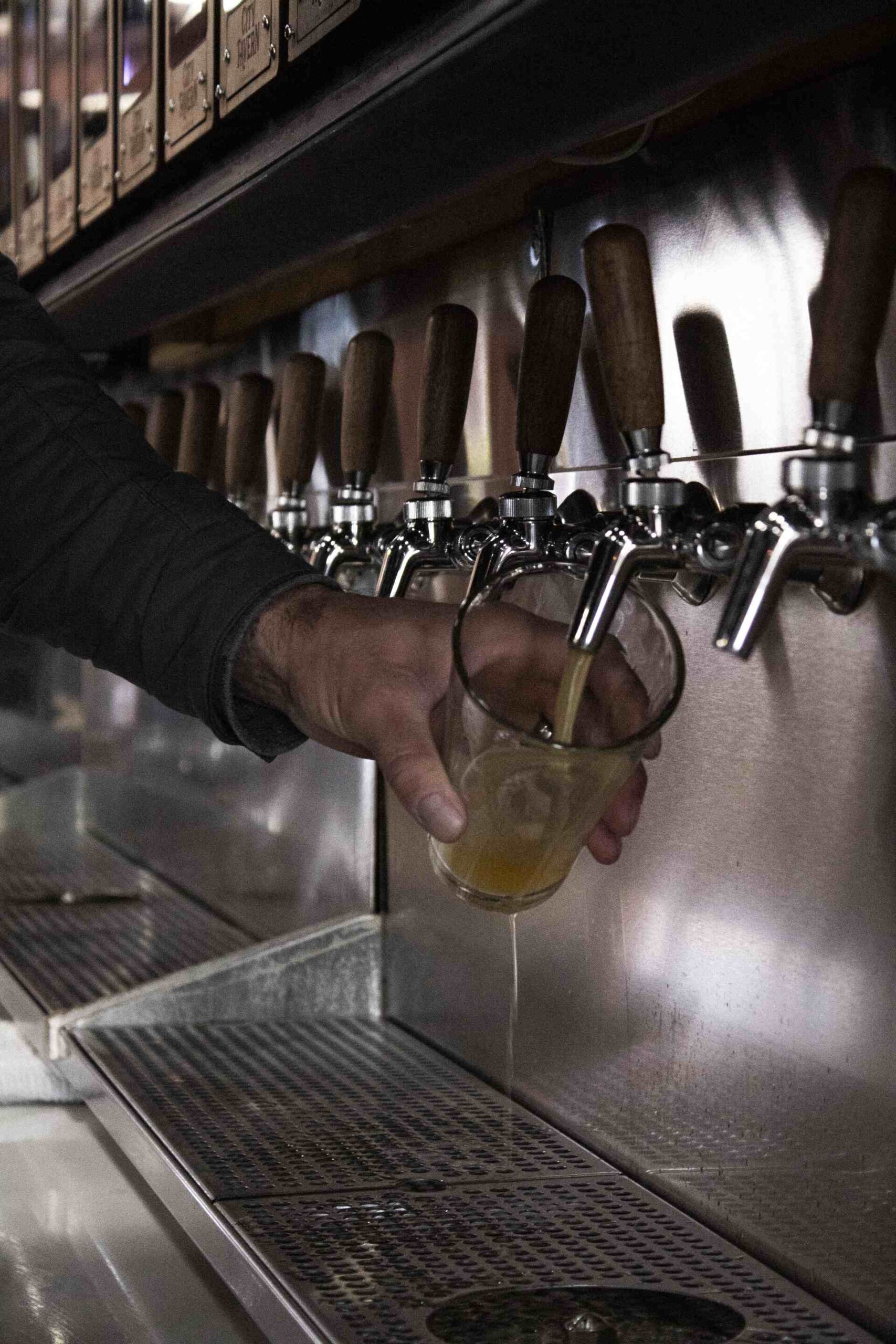 Person pouring draft beer from a tap into a glass at a self-serve tap wall