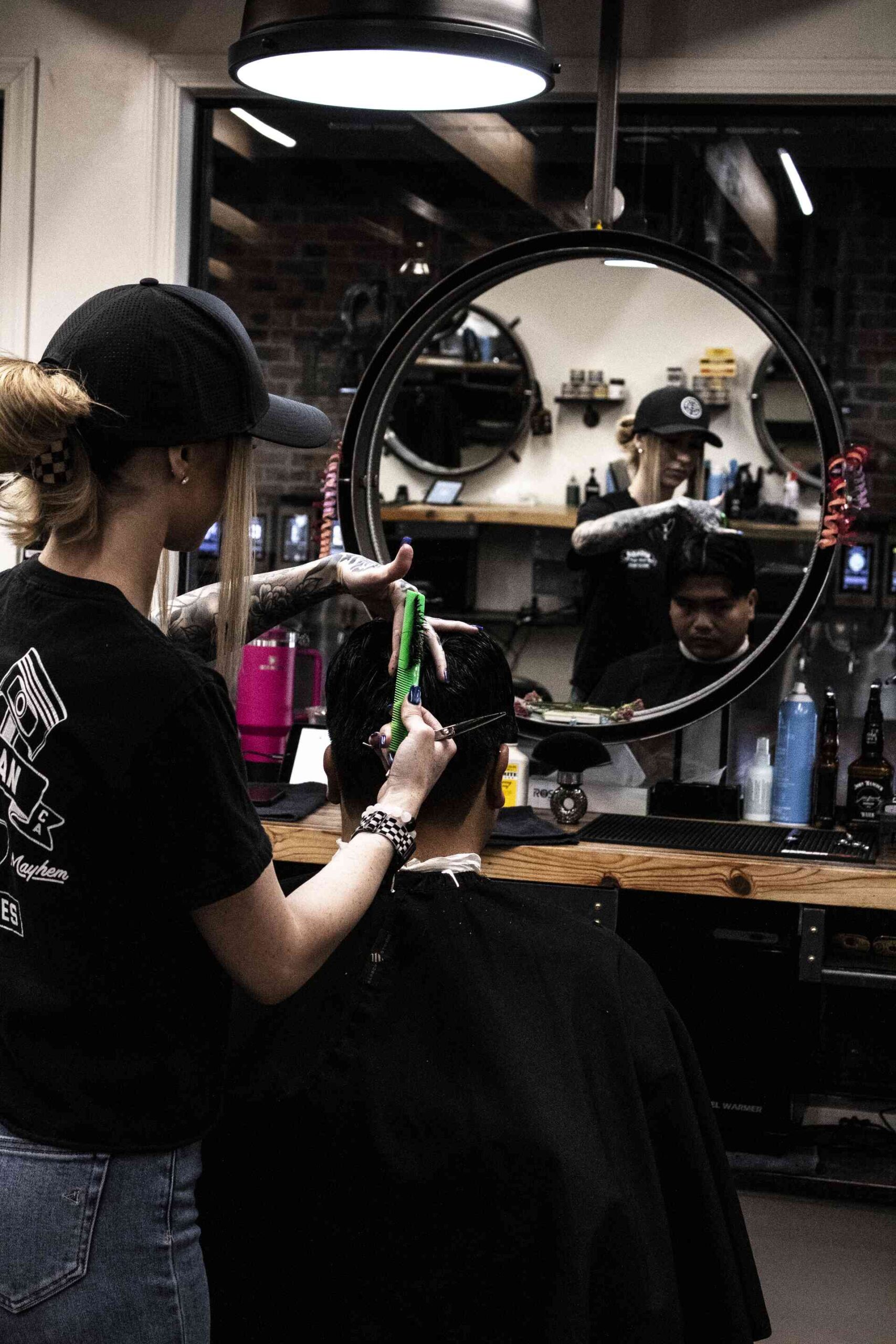 John Hackock Barber – Founding Fathers_ Barber cutting a client’s hair at John Hancock Barbershop, reflected in a round mirror