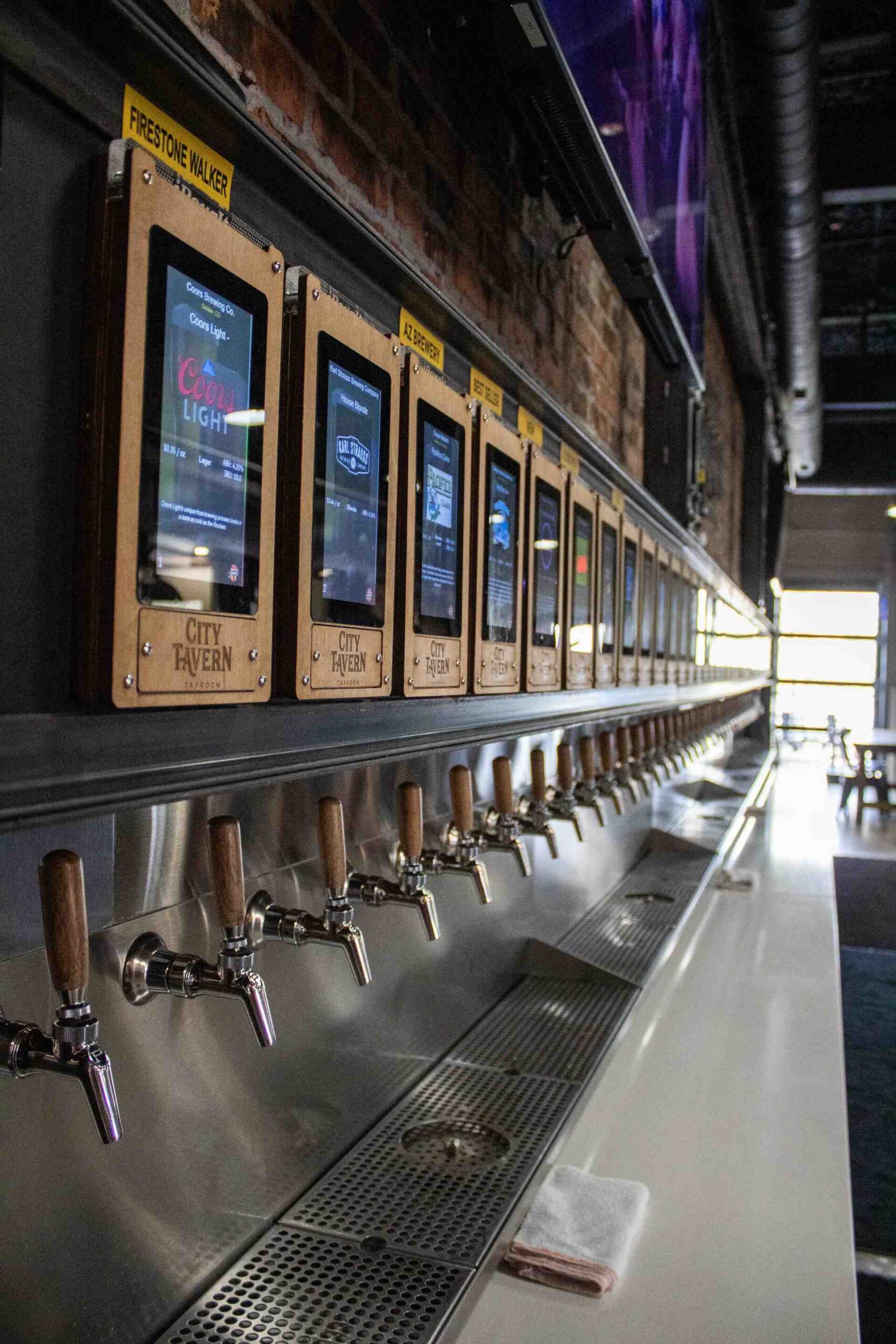Self-serve beer tap wall with digital screens and wooden handles at City Tavern