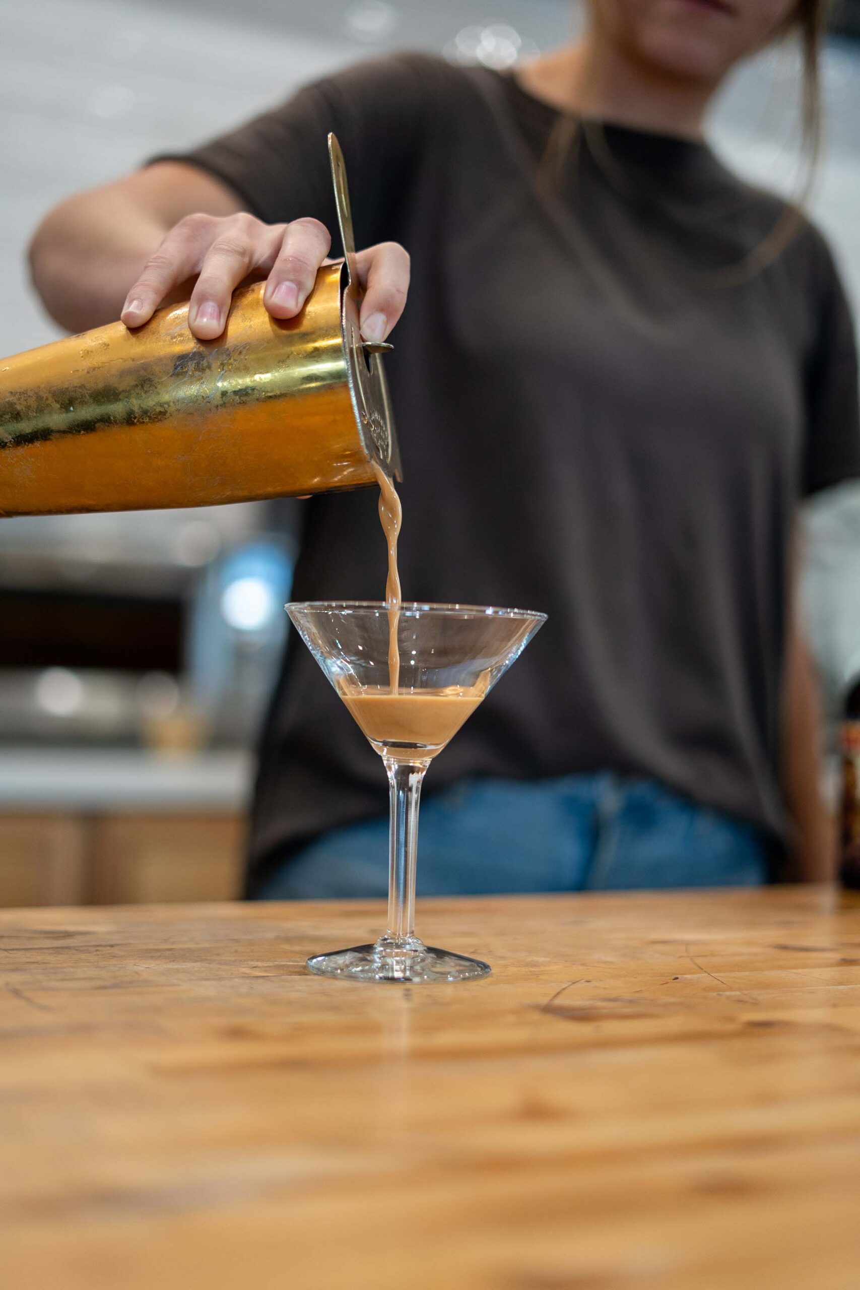 Merchant Coffee Martini Espresso shot pouring from a commercial espresso machine into a clear glass shot glass on a metal drip tray.