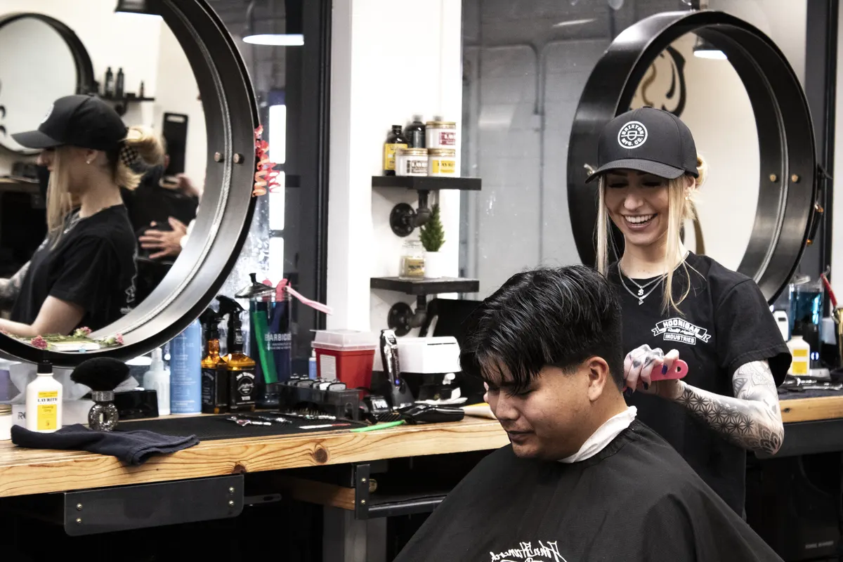 John Hancock Barbershops in Prescott—barber cutting a client’s hair under pendant lights while another barber preps a station.